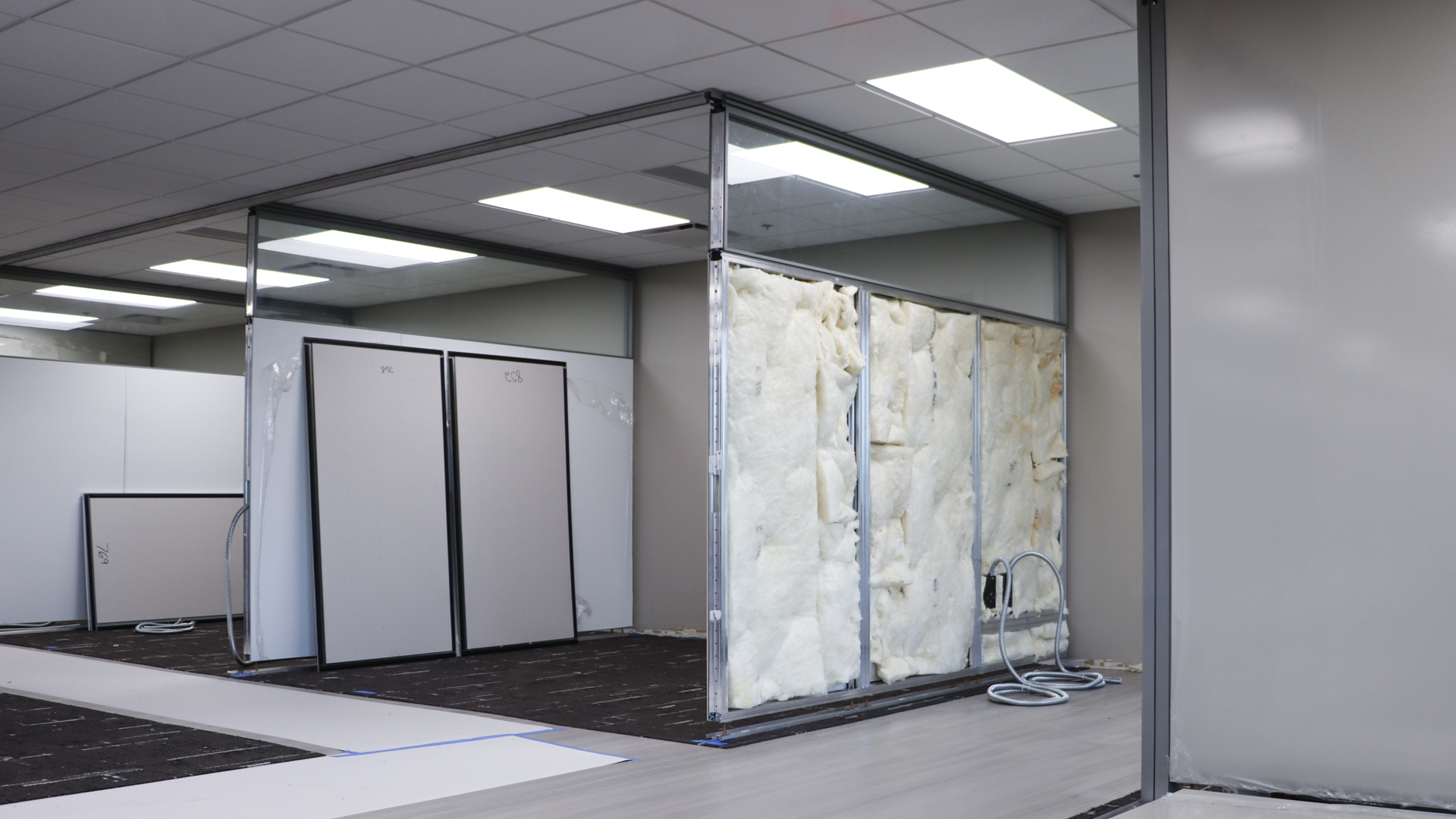 Architectural wall being installed, with insulation exposed and panels being set up in a modern office interior.
