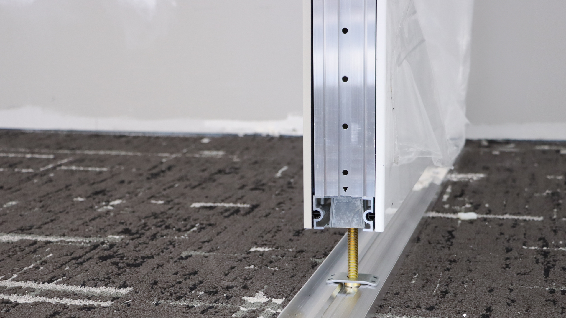 Close-up of an architectural wall panel anchored to a floor track with a screw.